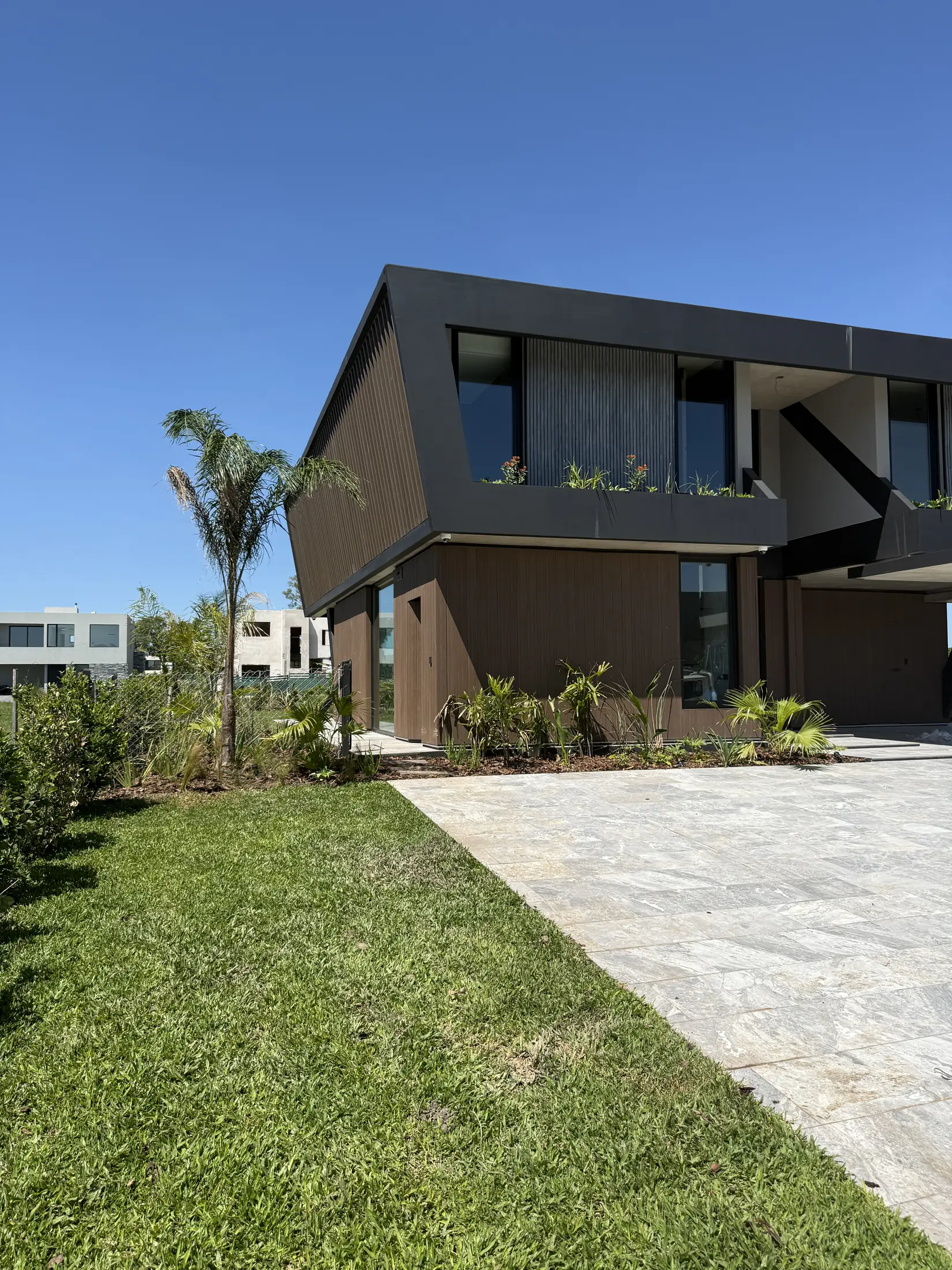 RB House de noche: el volumen superior de listones de madera, iluminado, vuela sobre el jardín